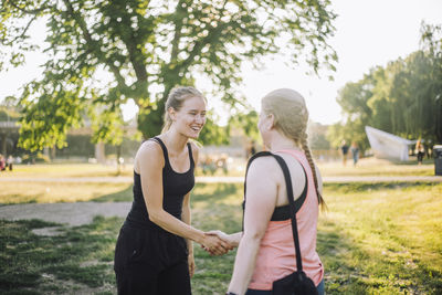 Smiling woman doing handshake with female friend at park