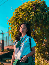 Young woman looking away while standing against plants