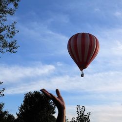 Cropped hand of person against hot air balloon in sky