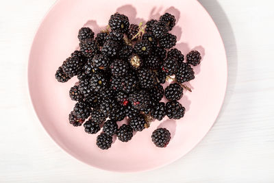 Fresh wild blackberries in plate on white wooden background. edible wild fruit