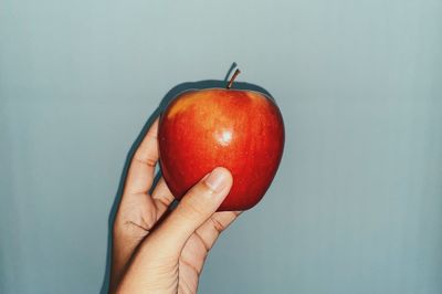 Close-up of hand holding apple against white background