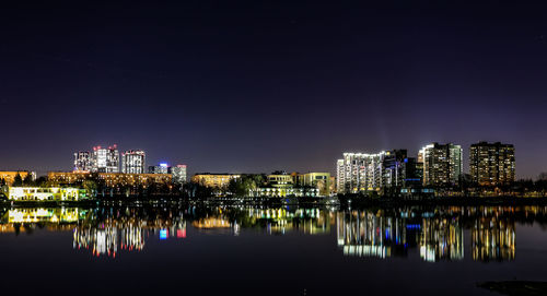 Illuminated buildings by river against sky at night