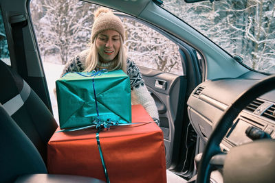 Woman giving gifts is holding presents delivering to home car holidays concept sunny cold winter day