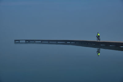 Reflection of cyclist on a lake pier against sky with fog