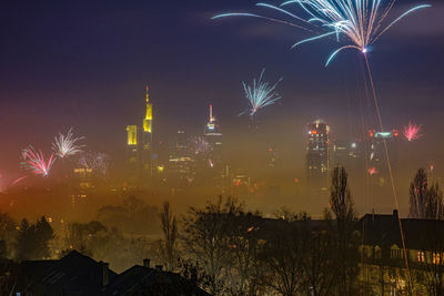 Firework display in city against sky at night