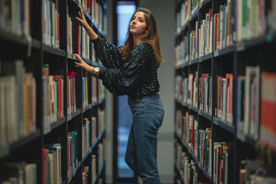 Side view of young woman looking at books in library