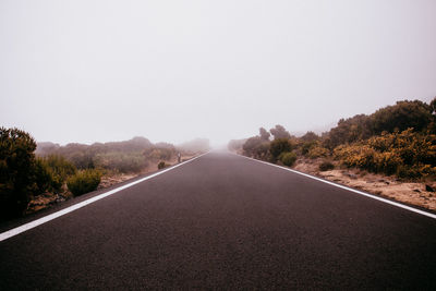 Empty road along trees and against clear sky