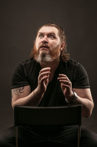 Portrait of man sitting against black background