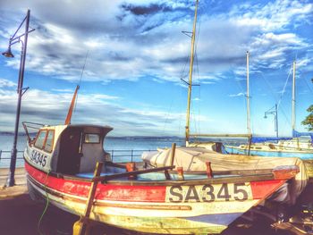 Boats in harbor against cloudy sky