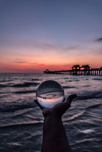 Close-up of hand against sea during sunset