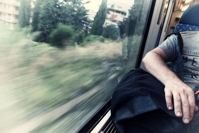 Cropped image of man sitting with luggage by window in train