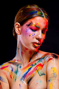 Shirtless young woman with colorful paints on her body against black background