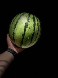 Close-up of hand holding watermelon  against black background