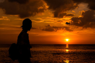 Woman standing at beach against sky during sunset