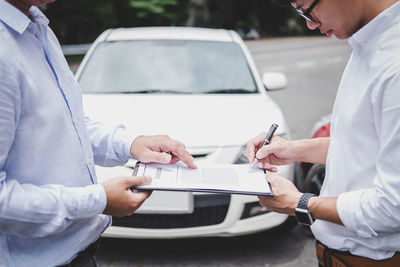 Midsection of agent giving documents to customer by car