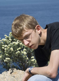 Thoughtful man sitting on rock by plants against sea