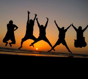 Silhouette people jumping on beach against clear sky during sunset