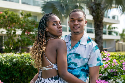 Portrait of a young couple standing against flowers while embracing