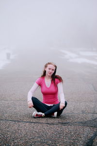 Portrait of smiling young woman sitting on bench against sky