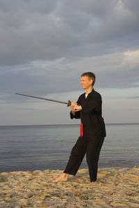 Man practicing tai chi at beach against cloudy sky