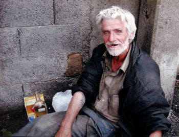 High angle portrait of senior man sitting against wall on street