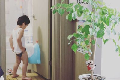 Side view of shirtless man standing by potted plant at home