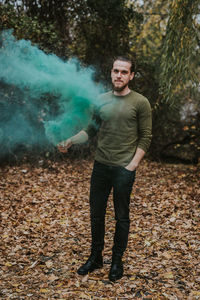 Portrait of young man holding distress flare while standing in forest during autumn