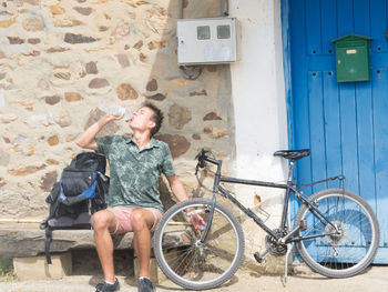 Young man with bicycle drinking water while sitting on seat