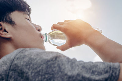 Portrait of young man drinking water against sky