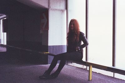 Full length of young woman sitting on railing at parking lot
