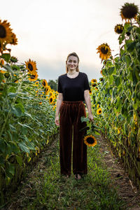 Portrait of young woman standing by plants against sky