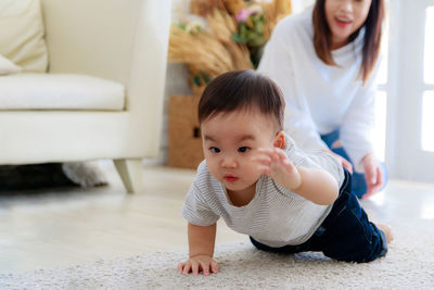 Mother looking at cute baby boy crawling on carpet