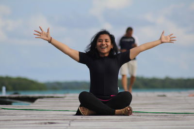 Young woman with arms raised against sky