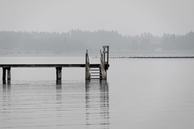 Wooden posts in lake against sky during winter