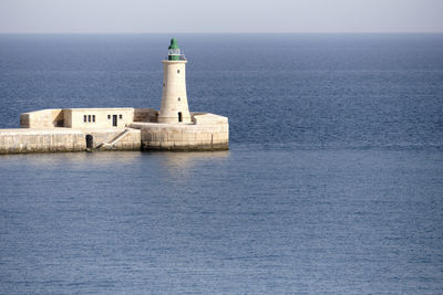 Lighthouse by sea against clear sky