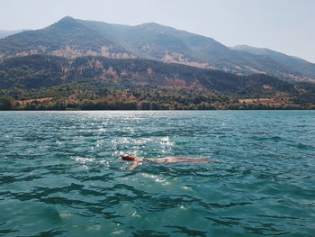 Young woman swimming in sea against mountain