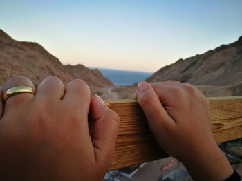 Close-up of hands on wood against clear sky during sunset