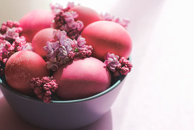 A grey bowl with bright pink easter eggs and lilac flowers on a purple background. easter decor