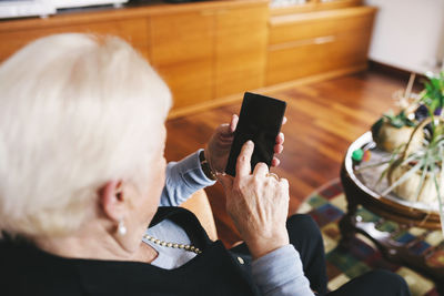 Senior woman sitting in the living room using smartphone