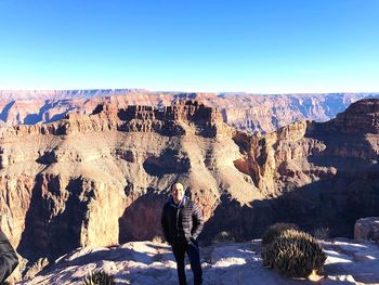 Man standing at rock formation against blue sky