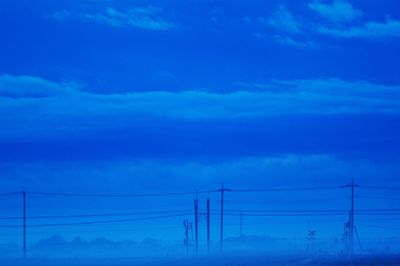 Low angle view of electricity pylon against blue sky