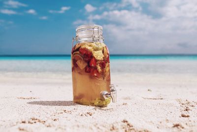 Close-up of jar on sand at beach against sky