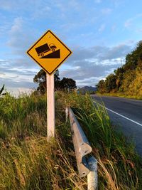 Information sign on road amidst field against sky