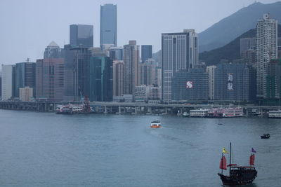 Sailboats in sea by buildings against sky in city