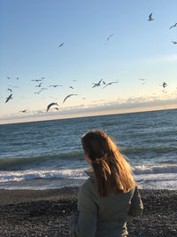 Rear view of woman standing at beach against sky during sunset