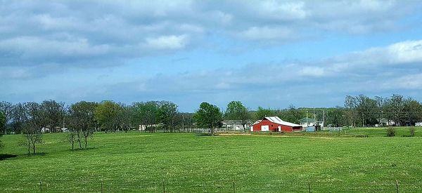 House on grassy field against cloudy sky