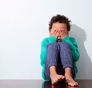 Full length of a boy covering face against white background stock photo