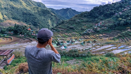 Rear view of man taking a photo of mountains