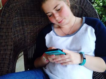 Woman using mobile phone while sitting on wicker chair outdoors