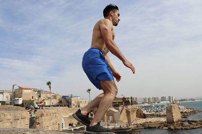 Side view of shirtless young man against sea and sky